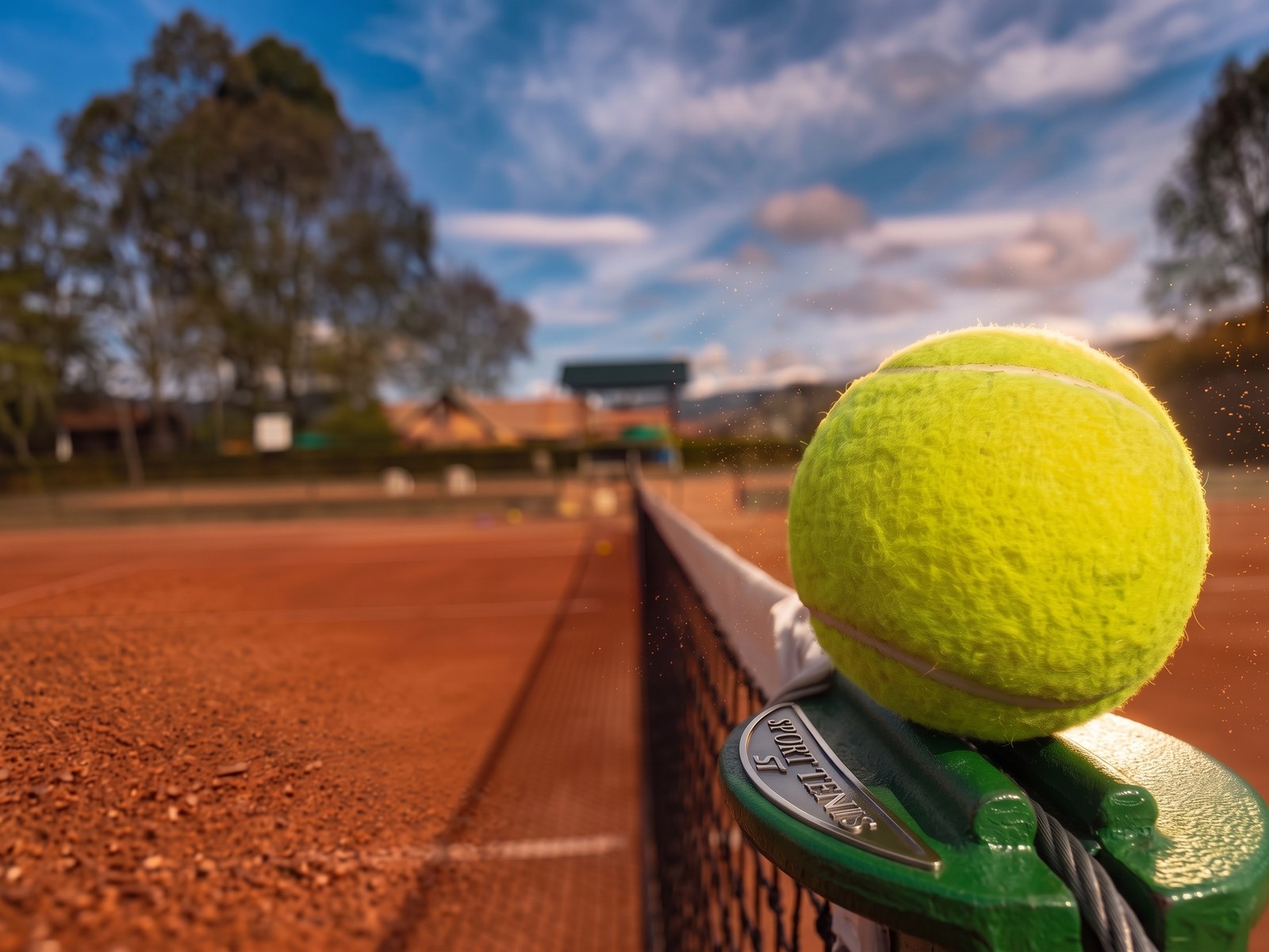 Pelota de tenis sobre la red, con la cancha de arcilla al fondo